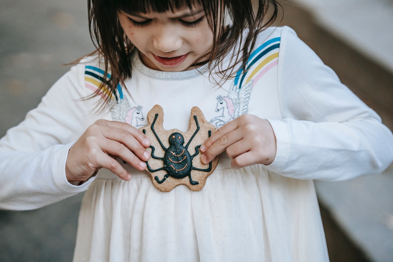 A girl holding a cookie with a spider decoration. 